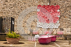 Stone wall, decorated with pink and white roses, and two pink bathtubs