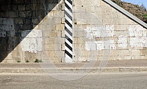 Stone wall at the entry of a road tunnel with erased graffiti . Sidewalk and road. Copy space