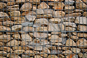 Stone wall of grindstone of light and gray color enclosed behind a metal grid.