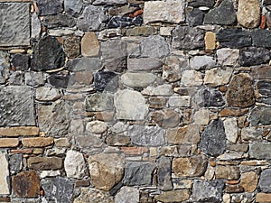 Stone wall made of irregular natural rocks of different sizes, bricks and slabs