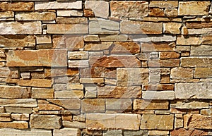 Stone wall with natural rock bricks of dfferent shapes. Colors are shades of brown, white and gray.