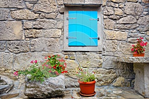 Stone wall of old house with blue window and flowers in pots. Hum, Croatia