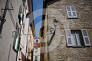 Stone wall of old house with windows with blue shutters, curtains drawn and vintage lantern on facade of building