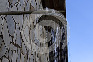 Stone wall with shower with falling water, outdoors in a swimming pool