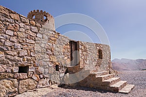 Stone wall of a small medieval arabian fort with wooden door and stone stairs in Bukha, Oman.