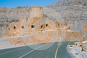 Stone walls of small medieval Arabian fort under tall mountain cliffs. Fortress in Bukha, Musandam peninsula, Oman. Hot