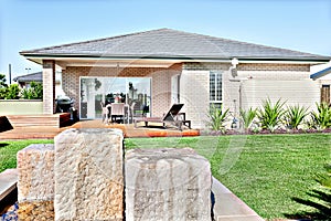 Stone water pond fixed to the lawn of a modern house with a wooden facade under blue sky