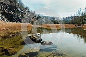 Stone in water in swamped quarry with high dry grass and rock, Czech republic