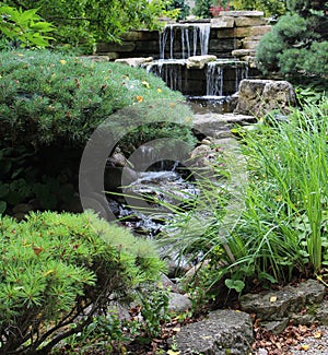 A stone waterfall cascading into a pond in a landscaped Japanese garden