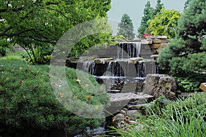 A stone waterfall cascading into a pond in a landscaped Japanese garden in Wisconsin