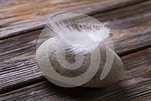Stone with white feather on wooden background.