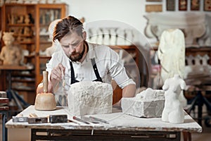 Stonemason which sitting in creative workshop and scraping the remains of lime-stone using brush