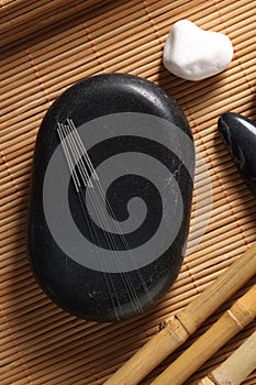 Stones with acupuncture needles on bamboo mat, flat lay