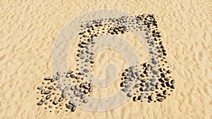 Stones on beach sand handmade symbol shape, golden sandy background, music sign