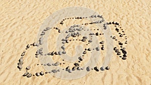 Stones on beach sand handmade symbol shape, golden sandy background, racing  car sign