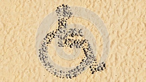 Stones on beach sand handmade symbol shape, golden sandy background, wheel chair sign