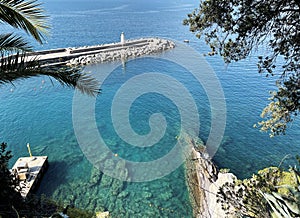 Stones, breakwater. Lighthouse and shore of sea coast. Turquoise-blue composition, background for design. Ligurian sea
