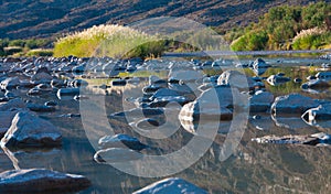 Stones covered with white salt in a shallow river, reflected in water.