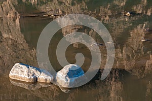Stones covered with white salt in a shallow river, reflected in water.