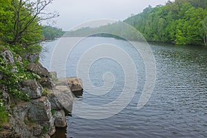 Stones near old rusty dam on a river at cloudy sky