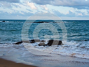 Stones one the beach with soft blue wave and cloudy sky