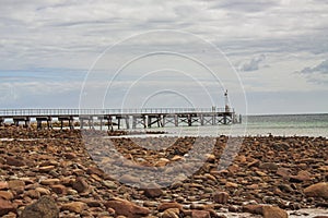 Stones scattered at the shore of Emu Bay with historic jetty during cast cloudy sky on Kangaroo Island in Australia. a