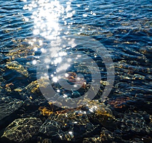 Stones under clear sea water, sun glare on the water