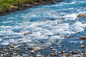 Stones in water riffle of mountain river. Powerful water stream among stones in mountain creek with rapids. Fast flow among rocks