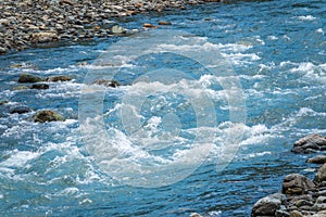 Stones in water riffle of mountain river. Powerful water stream among stones in mountain creek with rapids. Fast flow among rocks