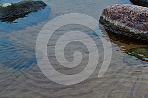 Stones with white stains on sandy shore with blue reflections in clear water of Lake Ladoga