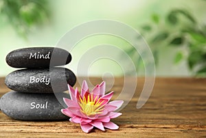 Stones with words Mind, Body, Soul and flower on wooden table, space for text. Zen lifestyle