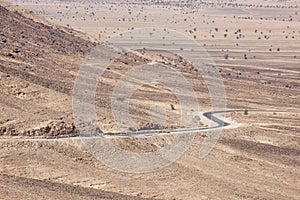 Stony desert landscapes with road and acacia trees.