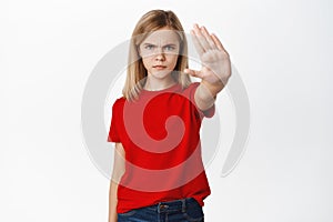 Stop. Angry little girl frowns, extends one hand palm to reject, prohibit, forbid smth bad, standing in tshirt over
