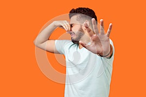 Stop bad smell. Side view of confused brunette man holding breath with fingers on nose. isolated on orange background