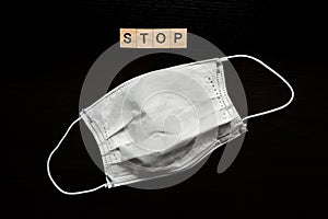 Stop coronavirus concept: `Stop` word and medical facial mask on dark