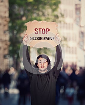 Stop discrimination, street manifestation protest. Man with hands outstretched holding a cardboard banner with warning message.