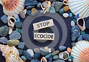 Stop ecocide symbol. Wooden blocks with words stop ecocide. Seashell and sea stones. Beautiful grey background, copy space.