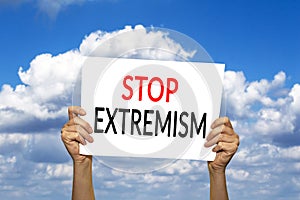 STOP EXTREMISM card in hand against blue sky with clouds.