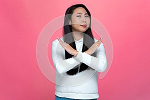 Stop gesture. Serious asian girl crossing hands, gesturing, prohibiting, restrict, reject, say no on pink background