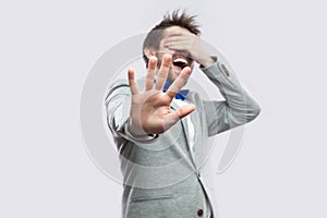 Stop, i don`t want to see this. Portrait of shocked or scared young bearded man in casual grey suit standing closed eyes and