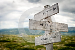 stop the madness text engraved on old wooden signpost outdoors in nature