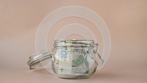 Stop motion of Polish zloty cash banknote collect in glass jar on beige background. Saving money concept crisis and