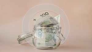Stop motion of Polish zloty cash banknote save in glass jar on beige background. Saving money concept crisis and