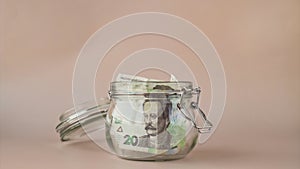 Stop motion of Ukrainian Hryvna cash banknote collect in glass jar on beige background. Saving money concept crisis and