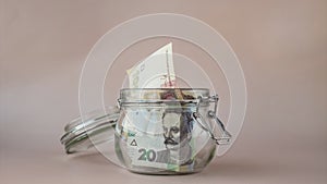 Stop motion of Ukrainian Hryvna cash banknote come in glass jar on beige background. Saving money concept crisis and
