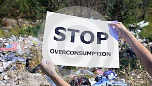 Stop overconsumption phrase on cardboard in hands against landfill background photo