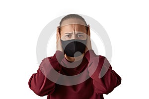 Stop please. Frowning young european woman wears face mask and burgundy sweatshirt, closes ears with hands, does not want to hear