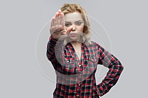 Stop. Portrait of serious beautiful blonde young woman in casual red checkered shirt standing with stop sign hand gesture and