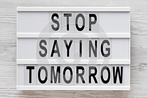 `Stop saying tomorrow` words on a lightbox on a white wooden background, top view. Overhead, from above, flat lay. Close-up