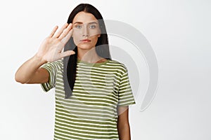 Stop it. Serious brunette woman stopping, showing block taboo gesture, saying no, standing in t-shirt over white